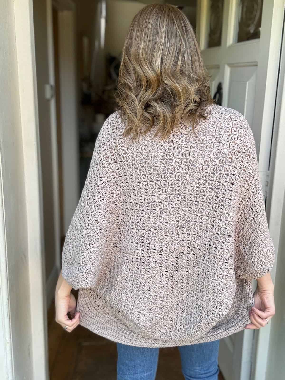 Back view of woman wearing oversized crochet cardigan standing in a doorway.