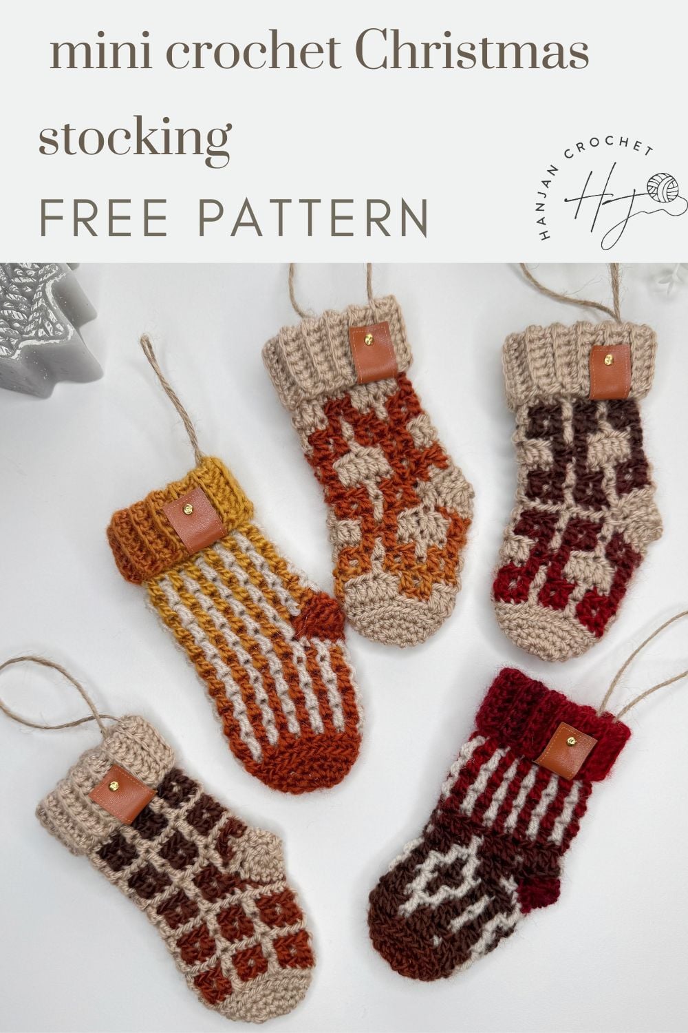 Five small crochet Christmas stockings in various patterns and earth tones are arranged on a white surface, each featuring a mini crochet Christmas stocking pattern, complete with a loop for hanging and a small leather tag on the cuff.