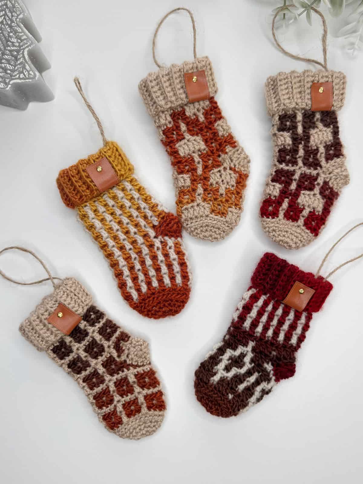 Five mini crochet Christmas stockings with assorted patterns and vibrant colors, each featuring a convenient hanging loop, are carefully arranged on a pristine white background.