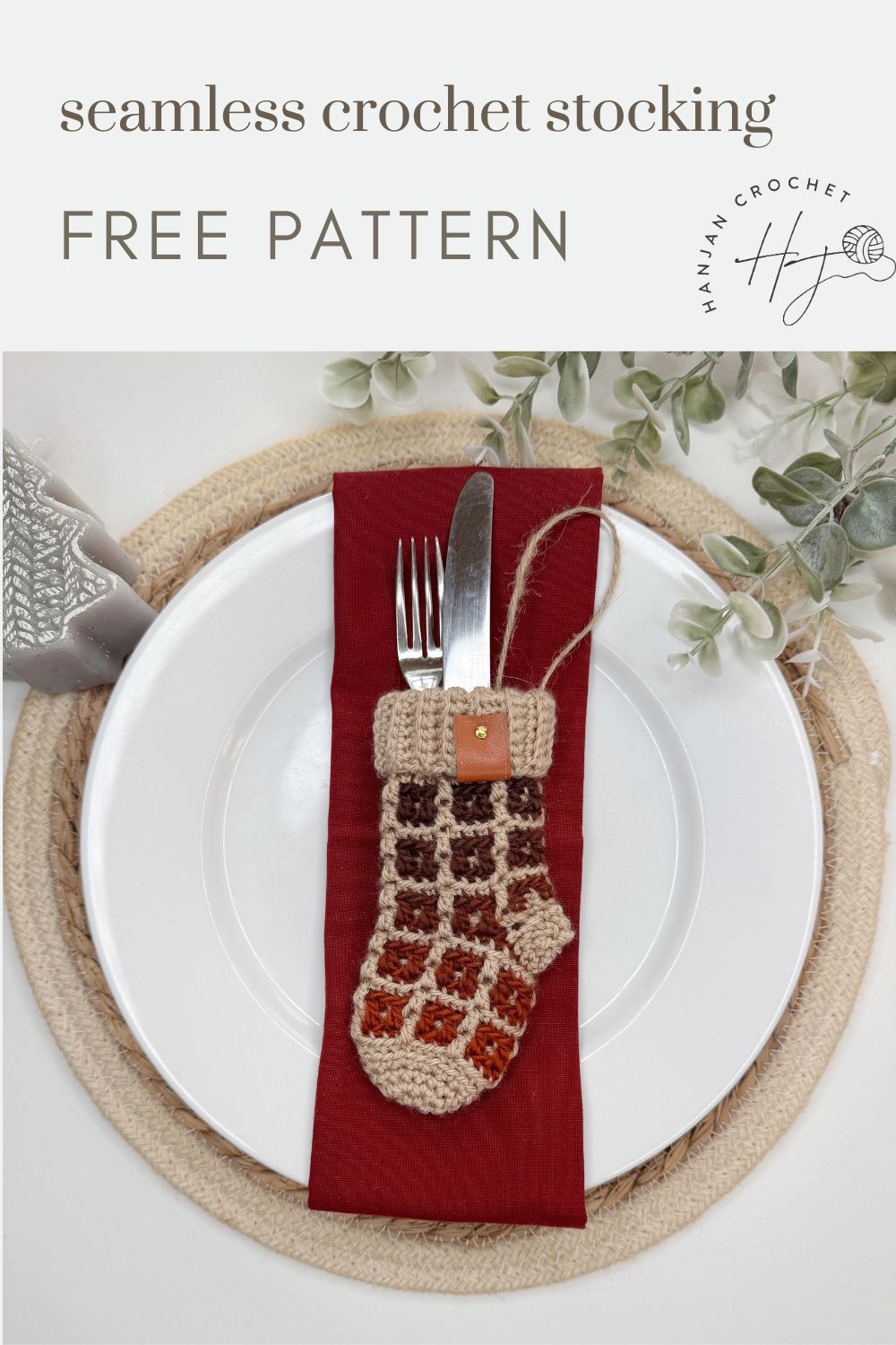 Place setting with a white plate, red napkin, fork, and knife tucked neatly into a small crochet stocking on top, surrounded by greenery, with text reading "seamless mini crochet Christmas stocking pattern FREE PATTERN".