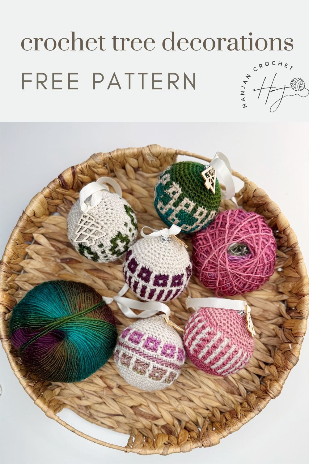A wicker basket holds five crochet tree decorations with geometric patterns, alongside two balls of yarn in green and pink shades.
