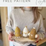 A person holds a wooden tray with three crocheted amigurumi chicks in yellow, white, and brown. This cute crochet chicken pattern is labeled as free from "Hannah Crochet.