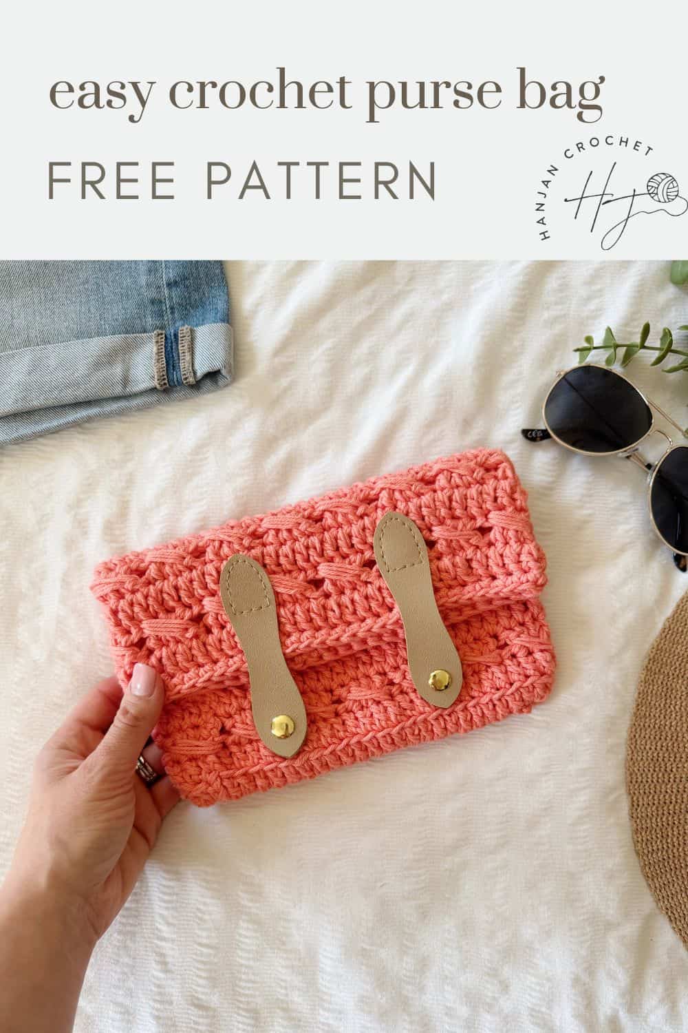 A hand holds a pink crocheted purse with tan straps on a white surface next to jeans, sunglasses, and a plant. Text above reads, "easy crochet clutch bag pattern FREE PATTERN.