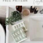Two crocheted facecloths with a green and white mosaic crochet pattern are folded and placed on a white bathroom sink beside a potted plant and several bottles—a lovely touch inspired by a mosaic crochet free pattern.