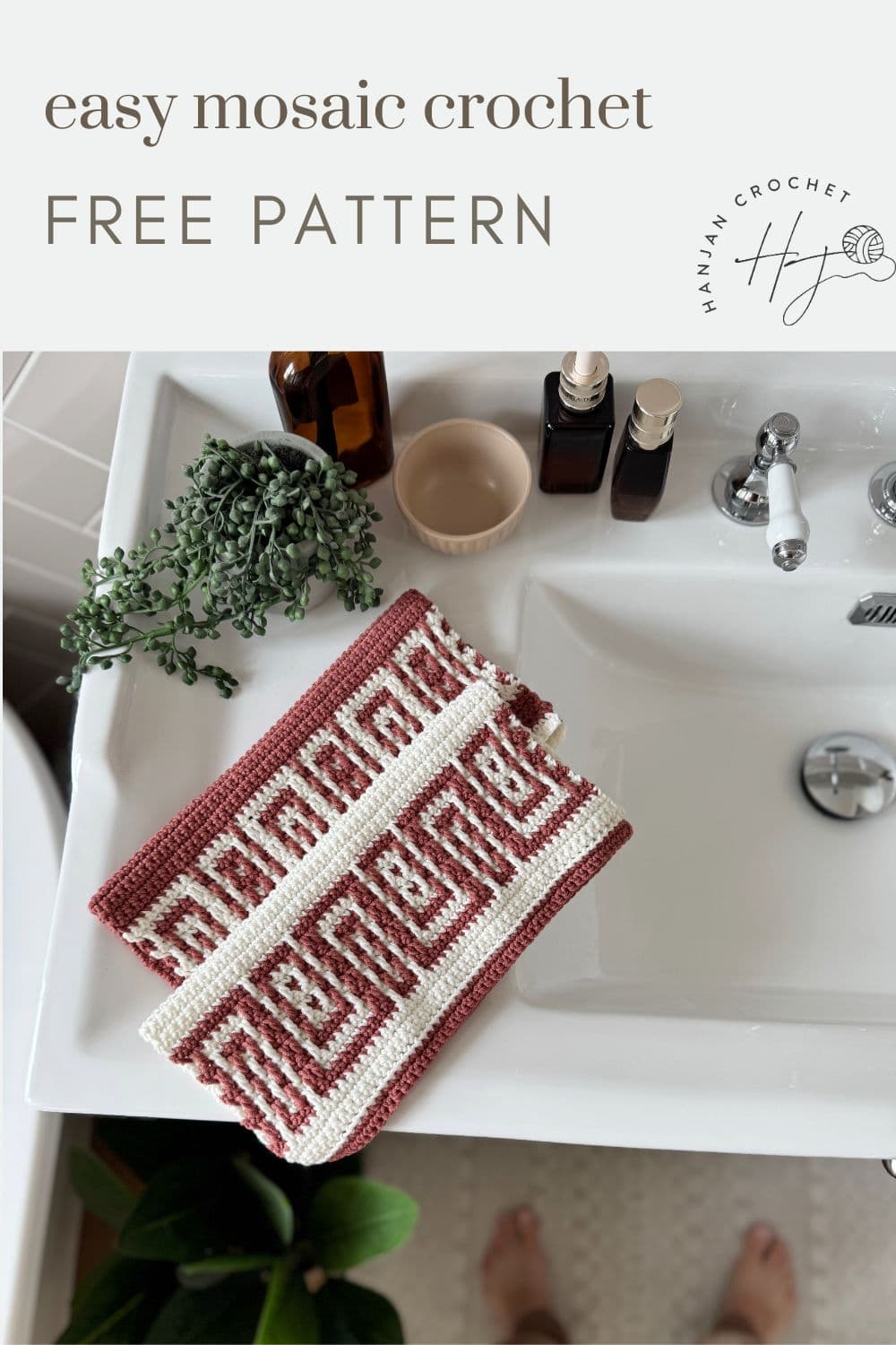 Two red and white mosaic crochet washcloths are folded on a white bathroom sink beside a plant and toiletries. Text reads: “easy free mosaic crochet pattern.”.