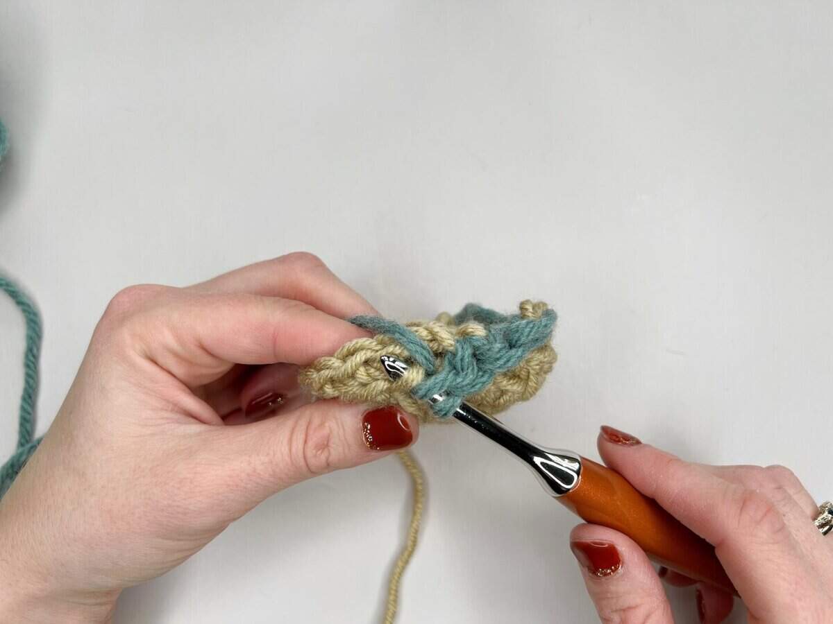 Close-up of hands crocheting with beige and teal yarn using a crochet hook, against a white background—perfect for illustrating a mosaic crochet tutorial.