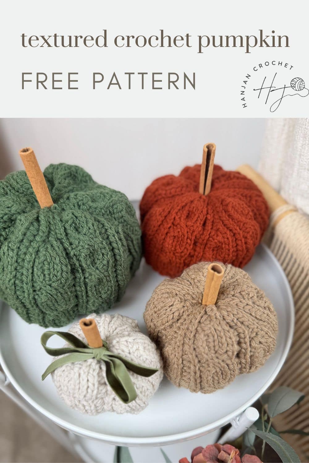 Four textured crochet pumpkins in green, orange, beige, and off-white with cinnamon stick stems displayed on a white tray; text reads "crochet pumpkin pattern free.