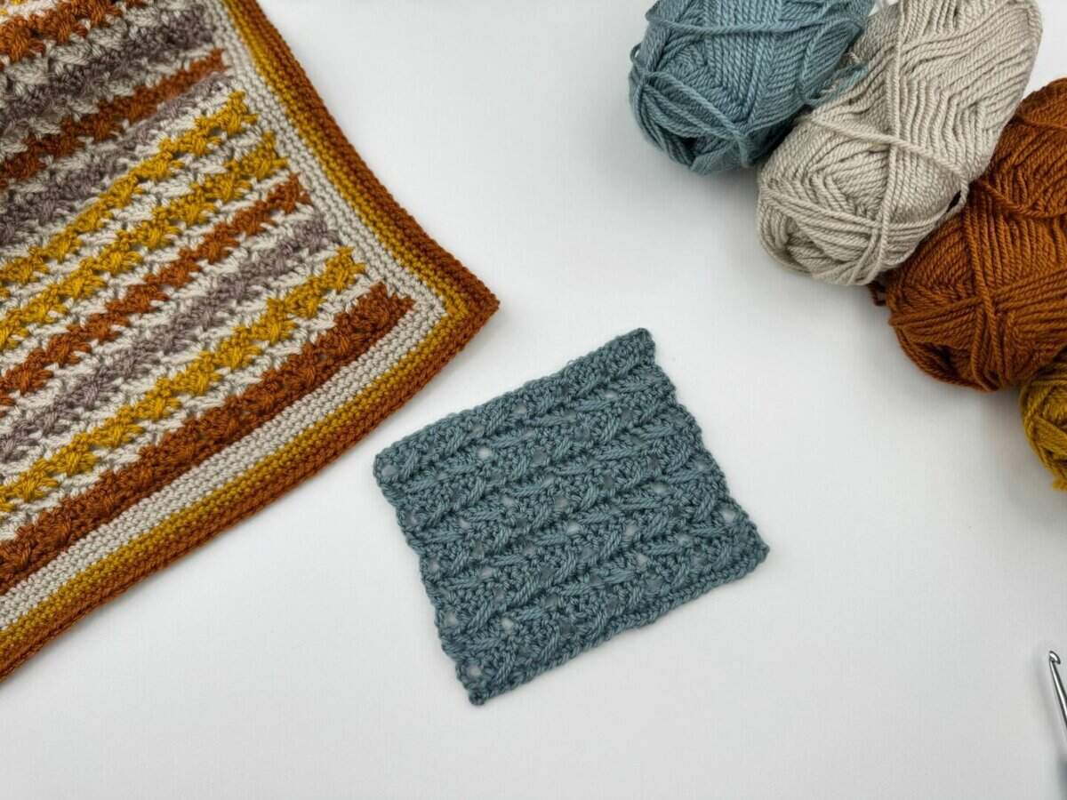 A blue crocheted swatch, made using the Crossover Stitch Crochet Tutorial, rests on a white surface beside a striped crochet piece and four balls of yarn in blue, beige, white, and brown.