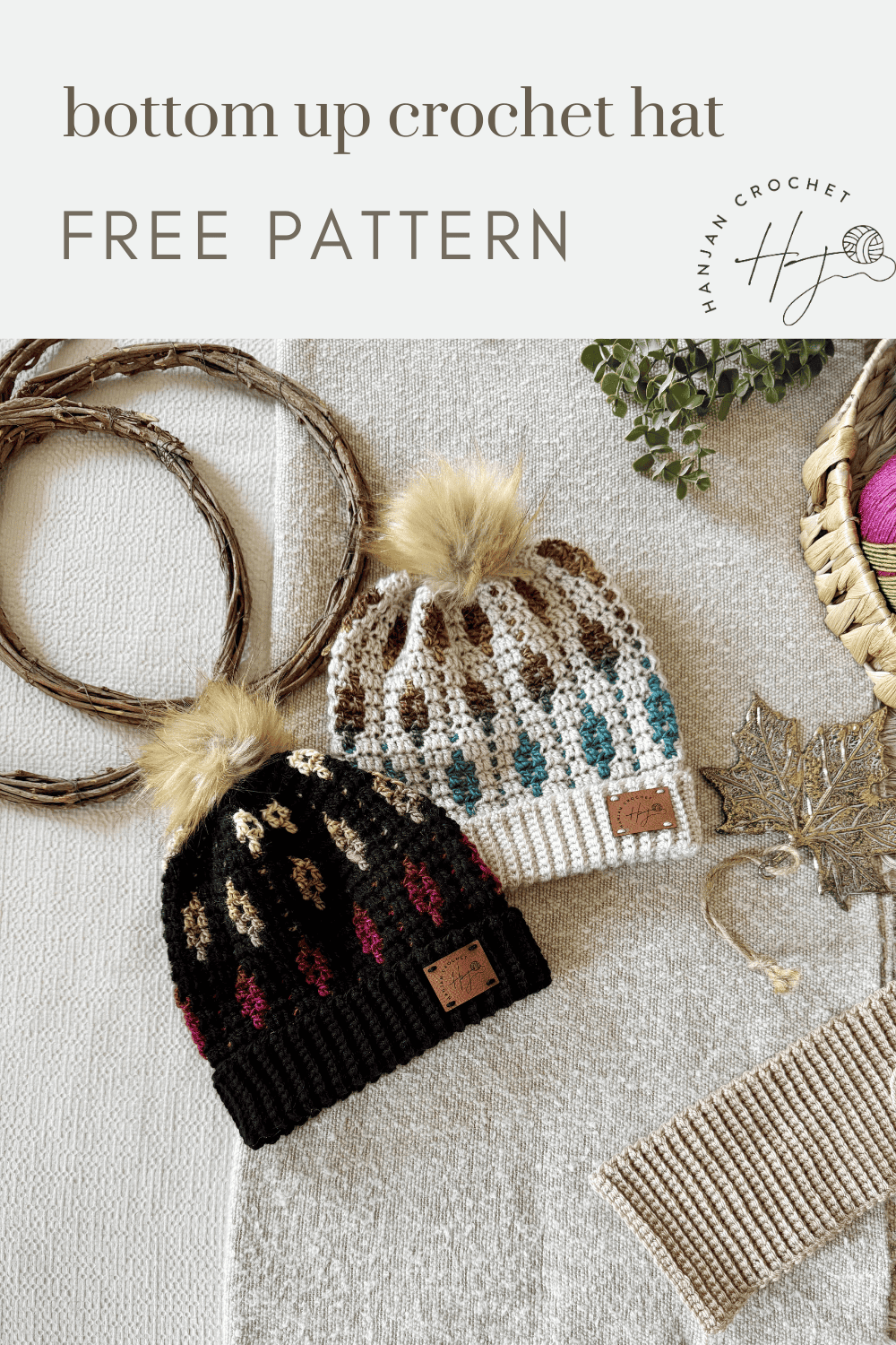 Two crocheted mosaic crochet beanie hats with pom-poms and leaf patterns, one in black and brown and one in cream and teal, are displayed with yarn and crochet supplies on a textured surface.