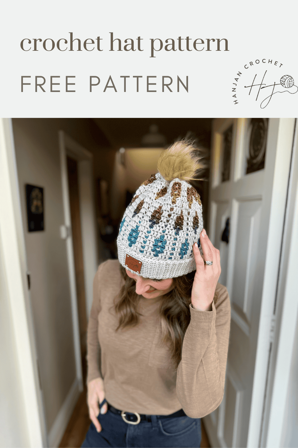 A woman wearing a crocheted hat with a pom-pom stands indoors beneath a sign reading "crochet hat pattern FREE PATTERN HanJan Crochet," showcasing her stylish mosaic crochet beanie.