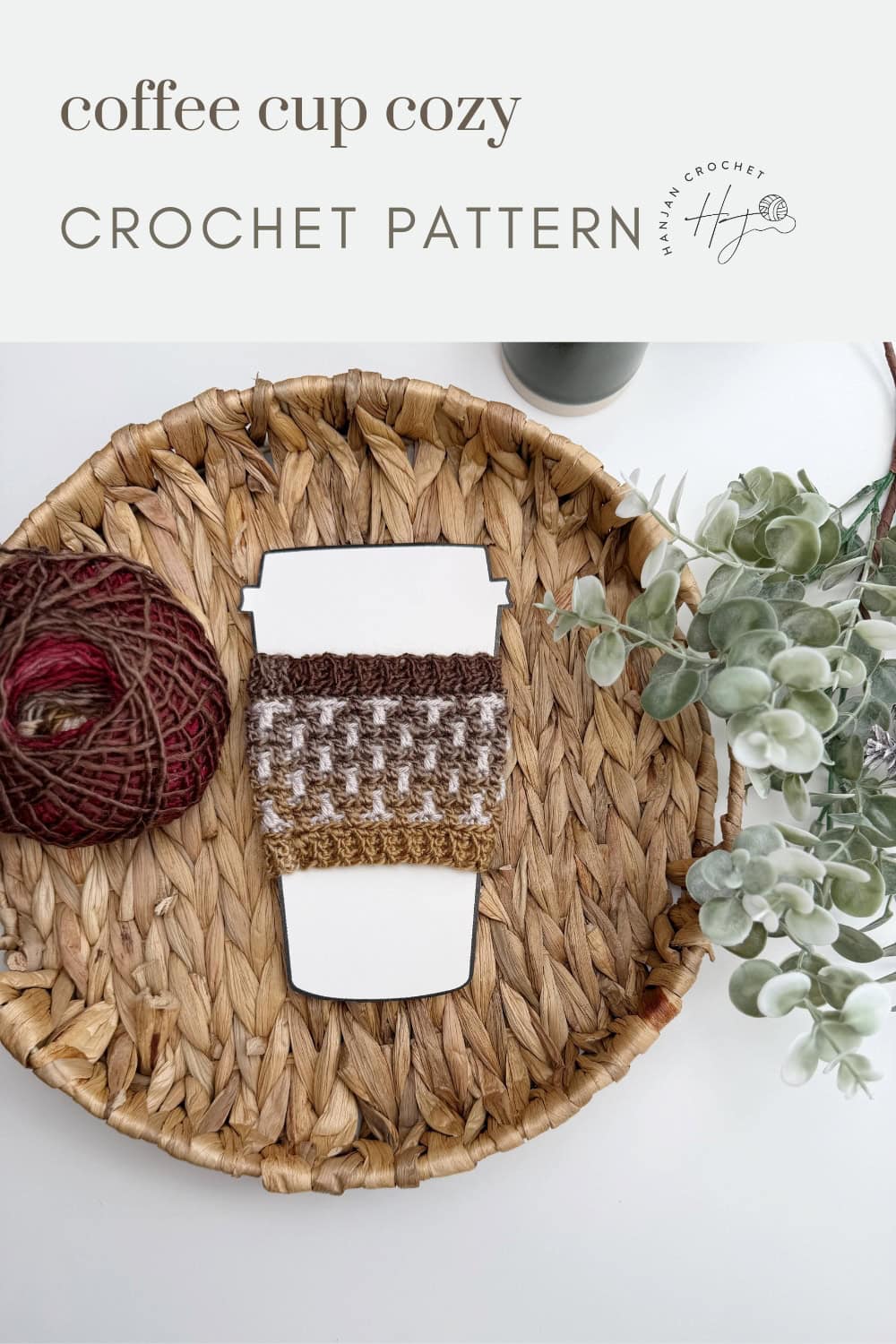A crochet coffee cup cozy displayed on a paper cup cutout, placed on a woven tray with a ball of yarn and greenery. Text above reads "coffee cup cozy CROCHET PATTERN." Perfect Crochet Coffee Sleeve Pattern for your favorite mug!.