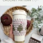 A hand holds a reusable cup with a crocheted sleeve featuring a green tree pattern. Yarn, crochet hook, and another Crochet Coffee Sleeve Pattern rest on a woven tray in the background.
