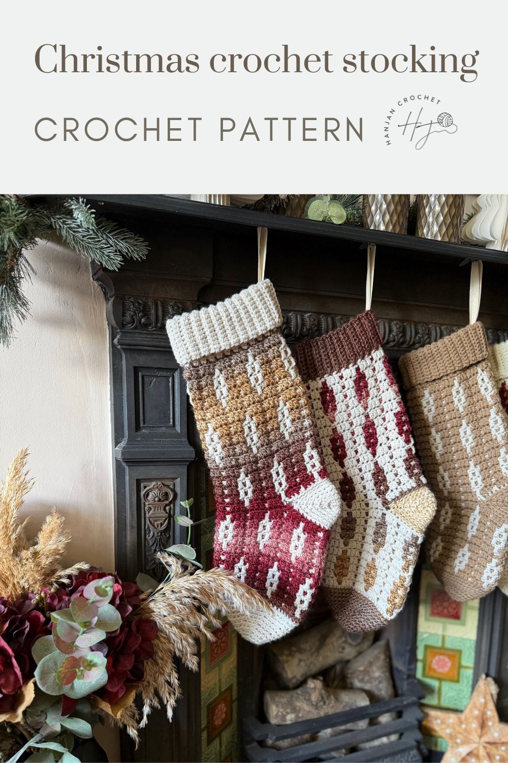 Three crocheted Christmas stockings in red, brown, and beige hang from a fireplace mantel adorned with greenery and dried flowers—perfect inspiration if you’re wondering how to crochet a Christmas stocking for your own festive décor.