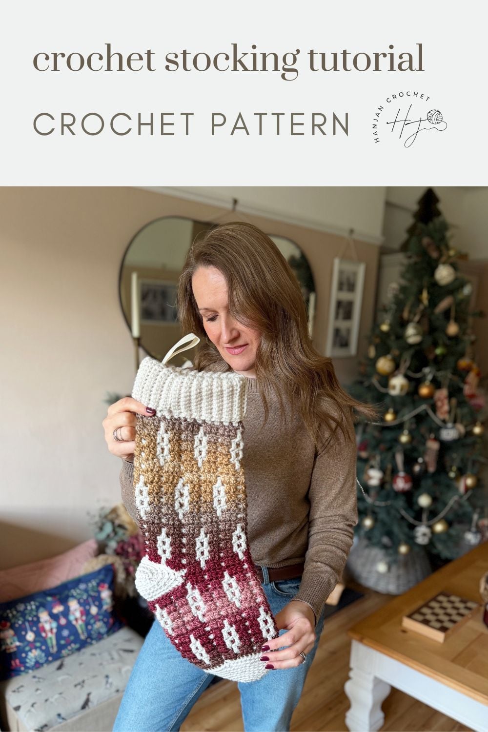 A woman holds a large crocheted Christmas stocking in a cozy living room with a festive tree behind her. Text reads "how to crochet a Christmas stocking - crochet stocking tutorial and pattern.