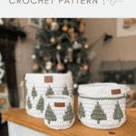 Three white christmas crochet baskets with green tree patterns are displayed on a table in front of a decorated Christmas tree, promoting a festive crochet pattern.