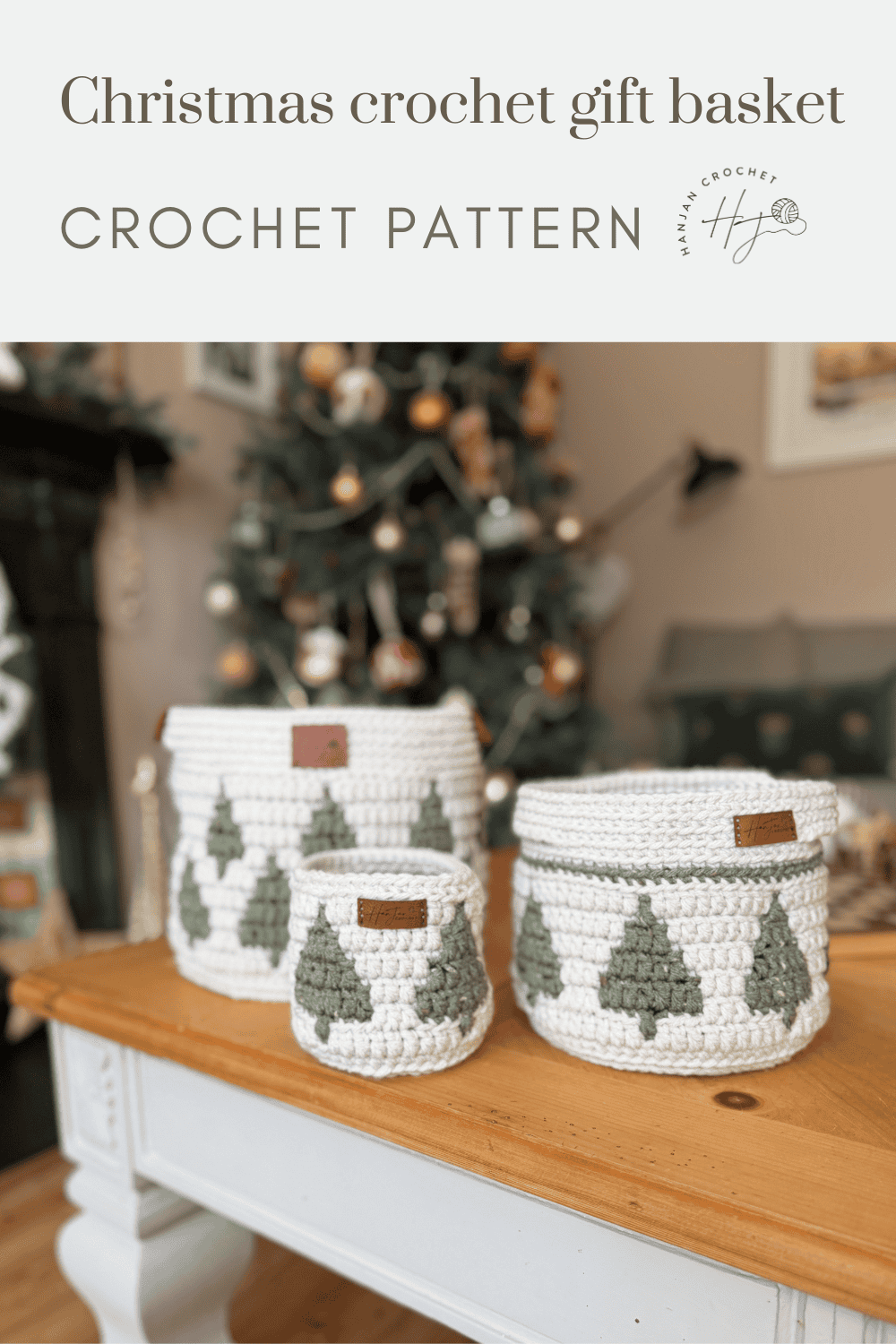 Three white christmas crochet baskets with green tree patterns are displayed on a table in front of a decorated Christmas tree, promoting a festive crochet pattern.
