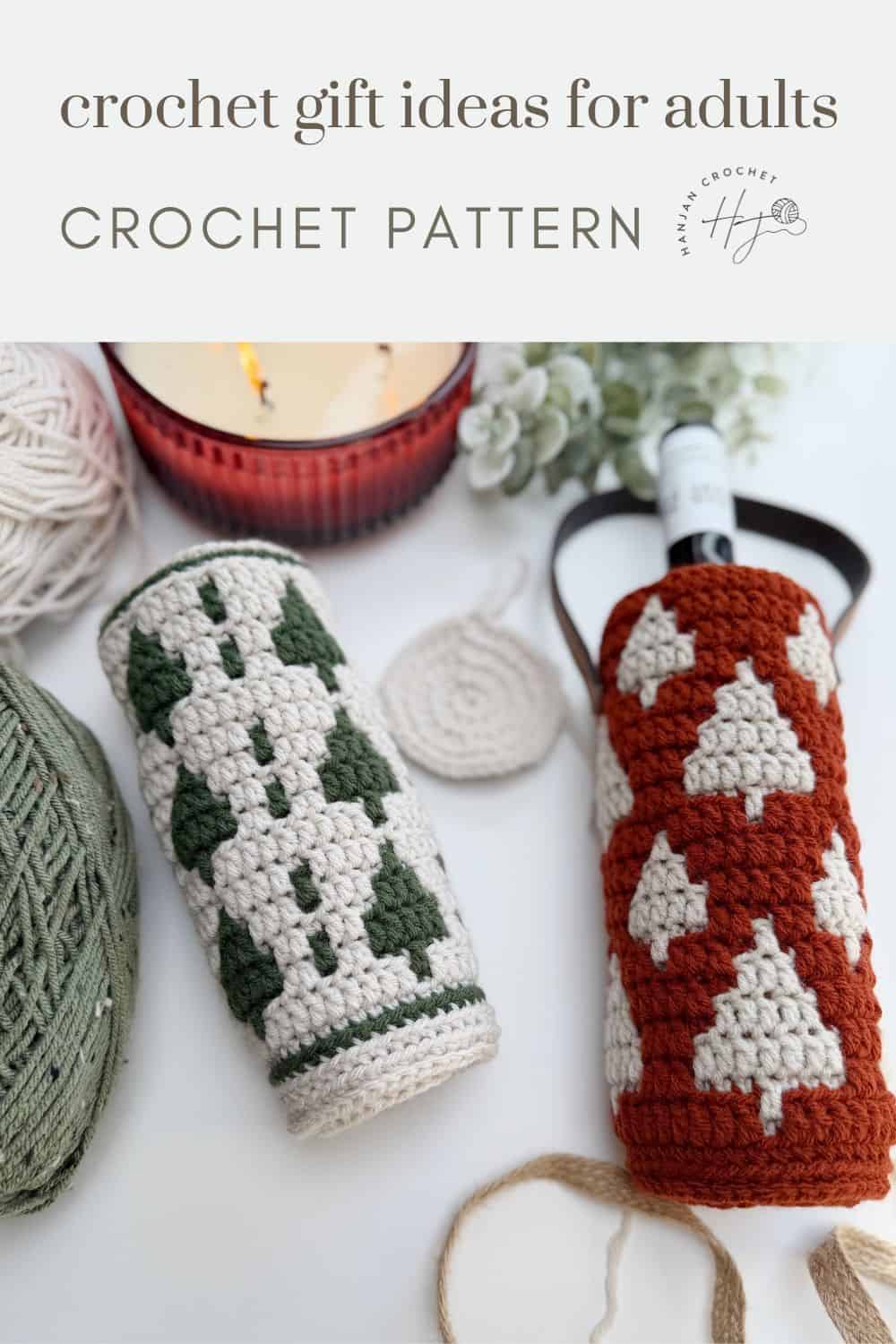 Two crochet wine bottle holders with tree patterns—one in green and white, the other in rust and white—are displayed alongside yarn, a candle, and a coaster.