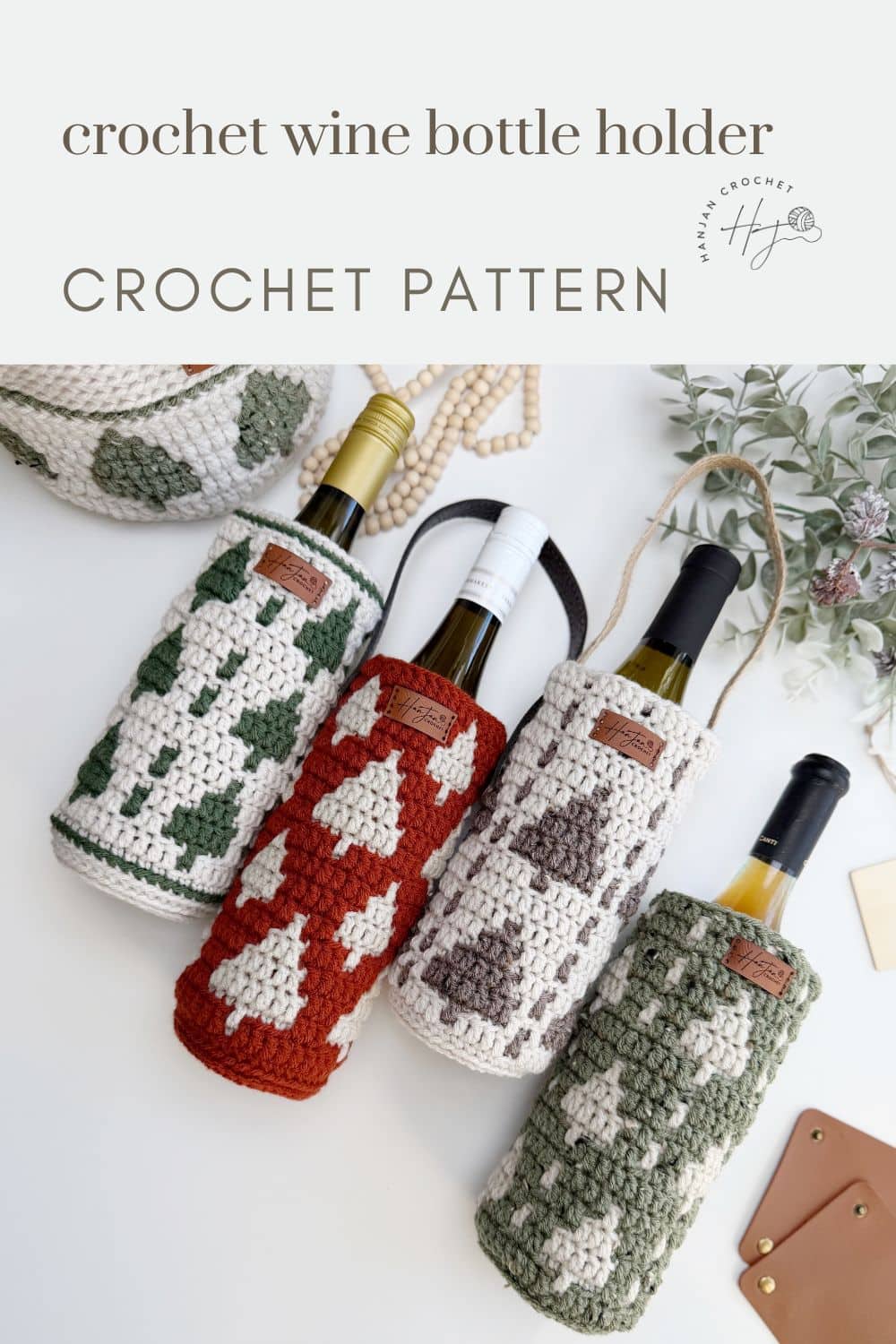 Four crochet wine bottle holders with geometric patterns in green, red, and cream colors, each holding a wine bottle, are displayed on a white surface.