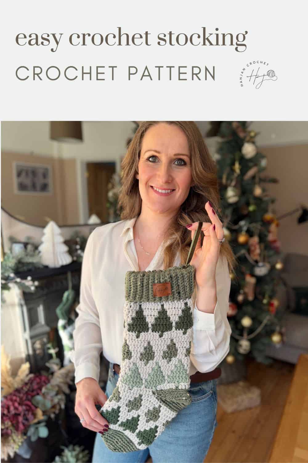 A woman stands indoors holding a crochet stocking pattern finished in green and white diamonds; a decorated Christmas tree is visible in the background.