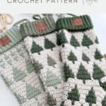 Three crocheted holiday stockings with green tree patterns and ribbed cuffs are displayed side by side against a neutral background. Text above reads "holiday crochet stocking CROCHET PATTERN," featuring a festive crochet stocking pattern.