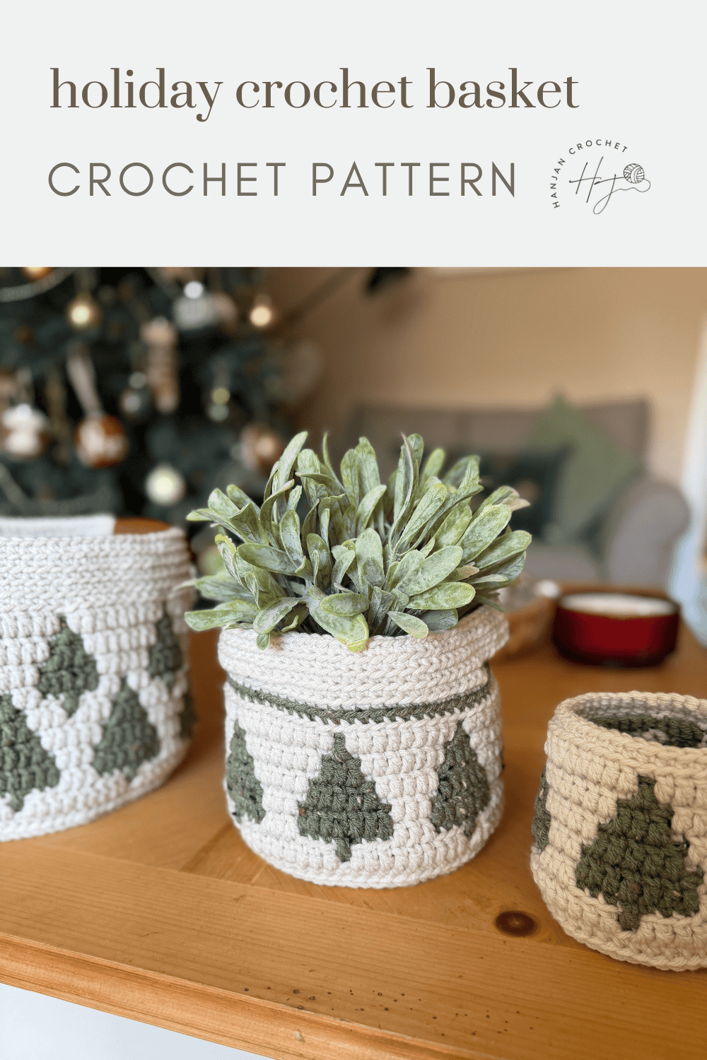 Three christmas crochet baskets with green tree patterns sit on a wooden table, one holding a potted plant. A decorated Christmas tree is visible in the background.