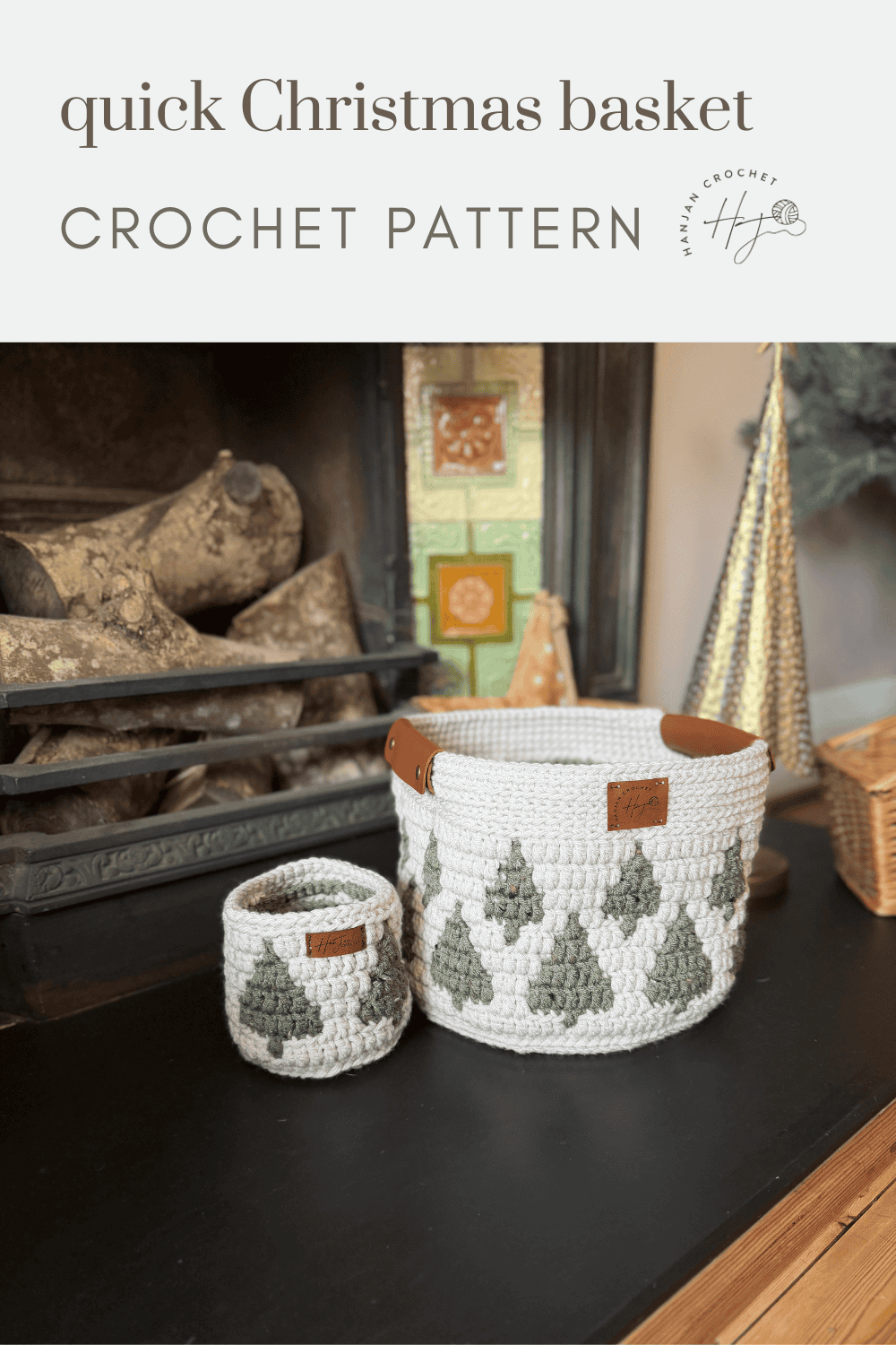 Two christmas crochet baskets with green Christmas tree patterns, one large with handles and one small, are displayed on a table in front of a cozy fireplace.