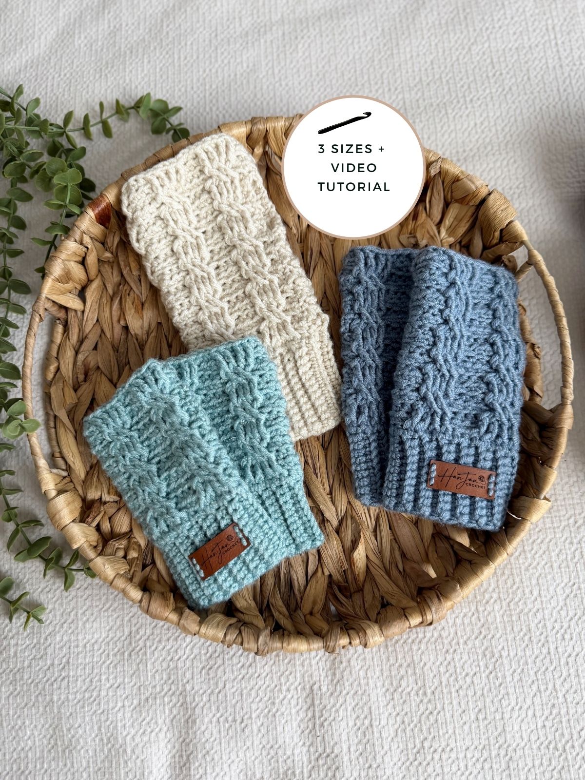 A woven basket holds three crocheted headbands in white, light blue, and blue-grey, each with a small brown label. A circular tag reads "3 sizes + video tutorial." Pair with our crochet wrist warmers free pattern for a cozy accessory set!.