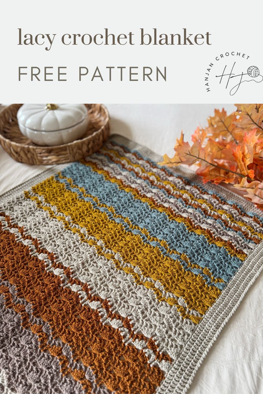 A multicolored lacy crochet blanket with mustard, blue, gray, and rust stripes is displayed on a table with a basket and autumn leaves. Text reads "lacy crochet blanket pattern free.