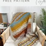 A striped crochet blanket in earthy tones and blue, featuring a lacy crochet blanket pattern, draped over a beige armchair with text offering a free pattern.