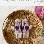 A pair of beige crochet heart mittens with purple heart patterns sits on a woven tray, next to a pink ball of yarn. Text above reads "crochet valentines gloves CROCHET PATTERN".