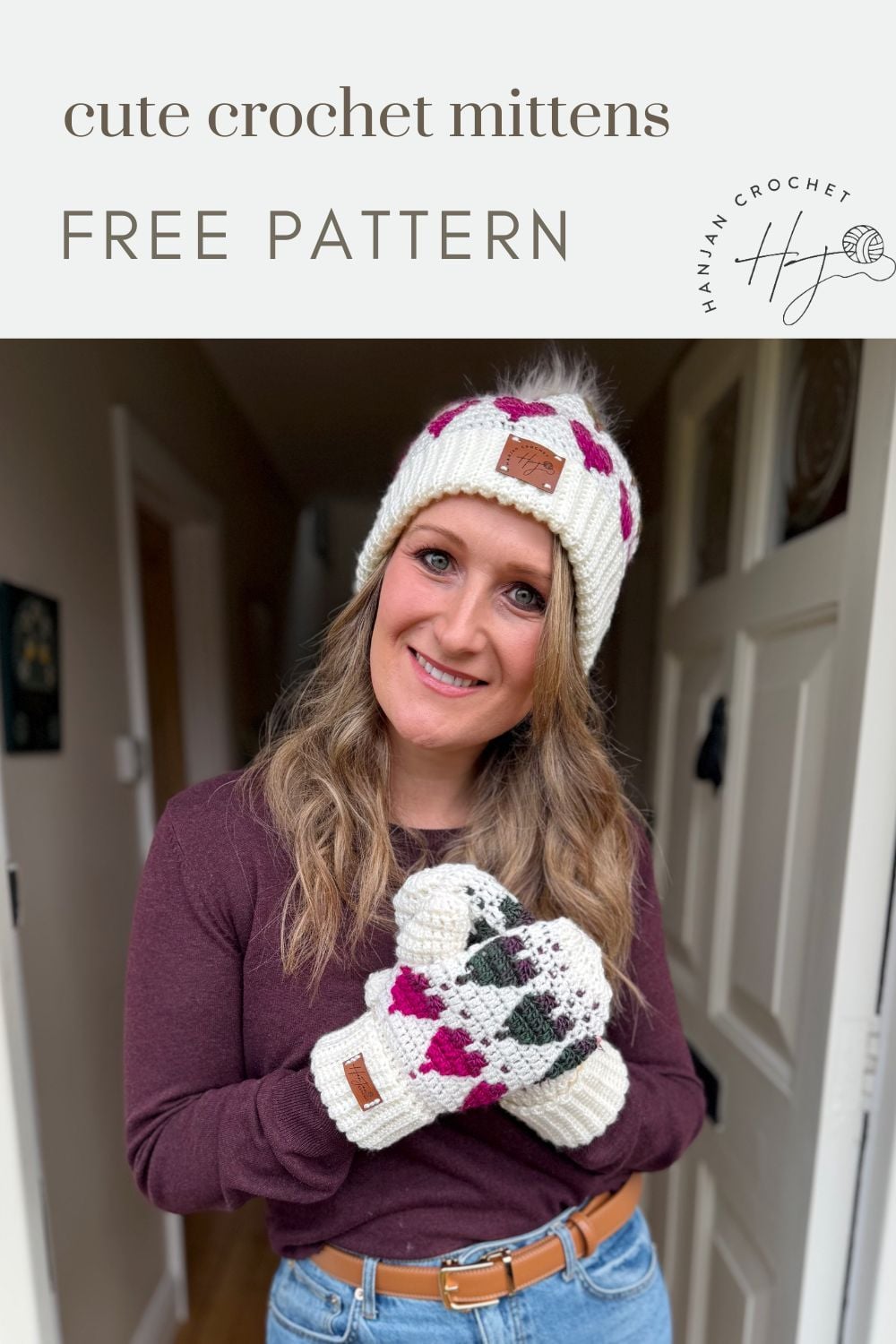 Woman wearing a white knit hat with a pom-pom and matching crochet heart mittens, standing indoors and smiling at the camera. Text reads "cute crochet mittens FREE PATTERN.