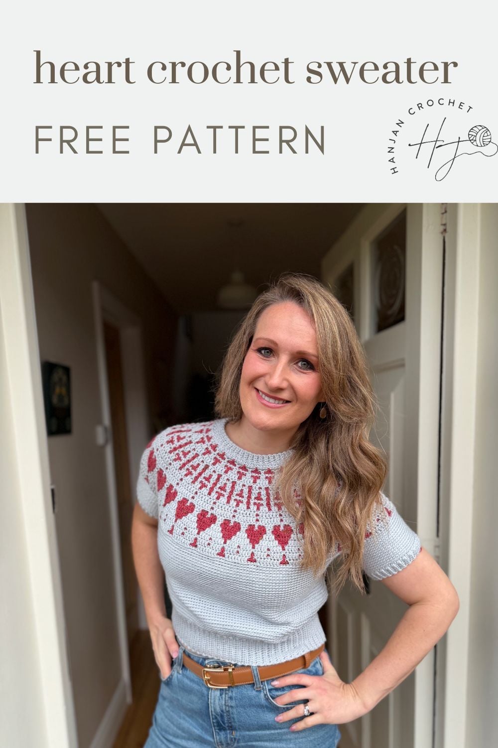 A woman stands in a hallway wearing a gray crochet sweater with a red heart pattern. Text above reads "heart crochet sweater FREE PATTERN" with a logo on the right.