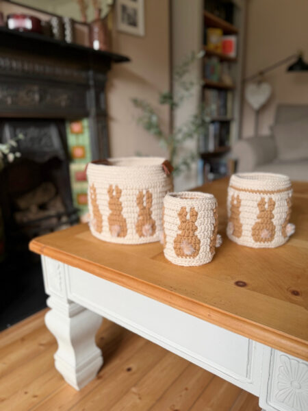 Three crocheted storage baskets with brown bunny designs sit on a wooden coffee table in a cozy living room.
