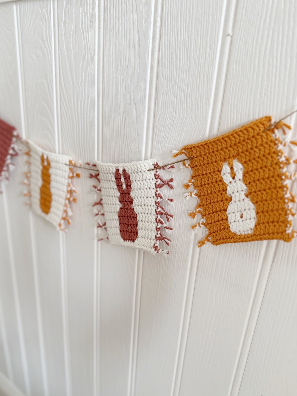 An Easter bunny crochet garland with crocheted squares featuring bunny silhouettes hangs against a white paneled wall.