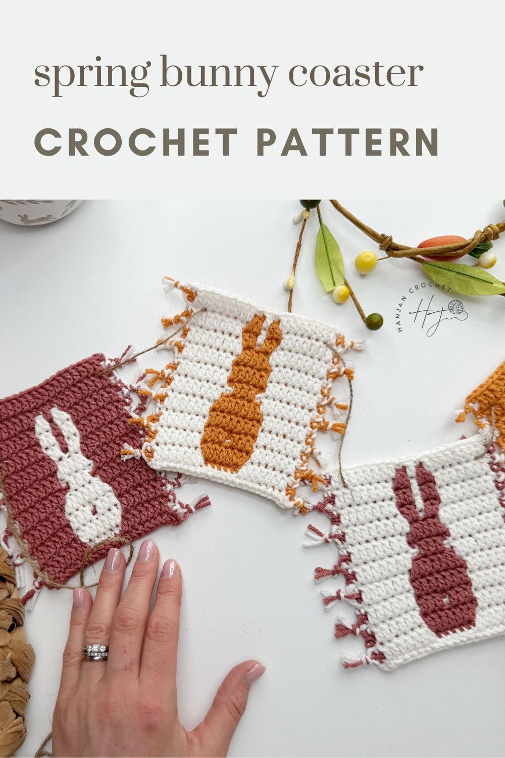 Three square crochet coasters feature bunny silhouettes in contrasting colors, displayed with a hand for scale and some decorative spring elements—perfect inspiration for your next crochet bunny coaster pattern.