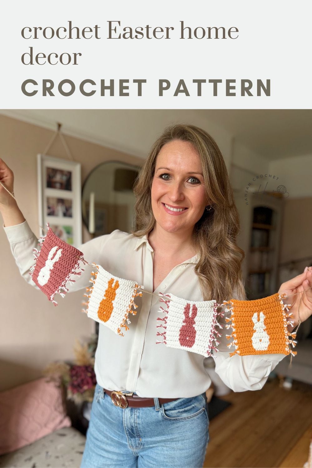 A woman holds a crochet Easter garland with bunny designs in pink, orange, and white squares, using the crochet bunny coaster pattern, standing in a living room.