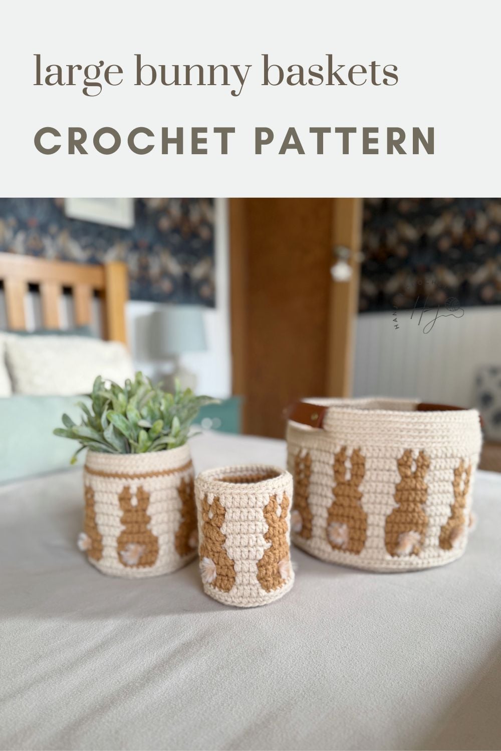 Three crocheted baskets of varying sizes, each featuring a bunny motif crafted from a crochet bunny basket pattern, are displayed on a bed next to a small potted plant.