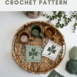 A woven tray holds three mugs and two crocheted clover coasters, with yarn and a finished crochet shamrock coaster nearby; text reads "crochet clover coaster CROCHET PATTERN.