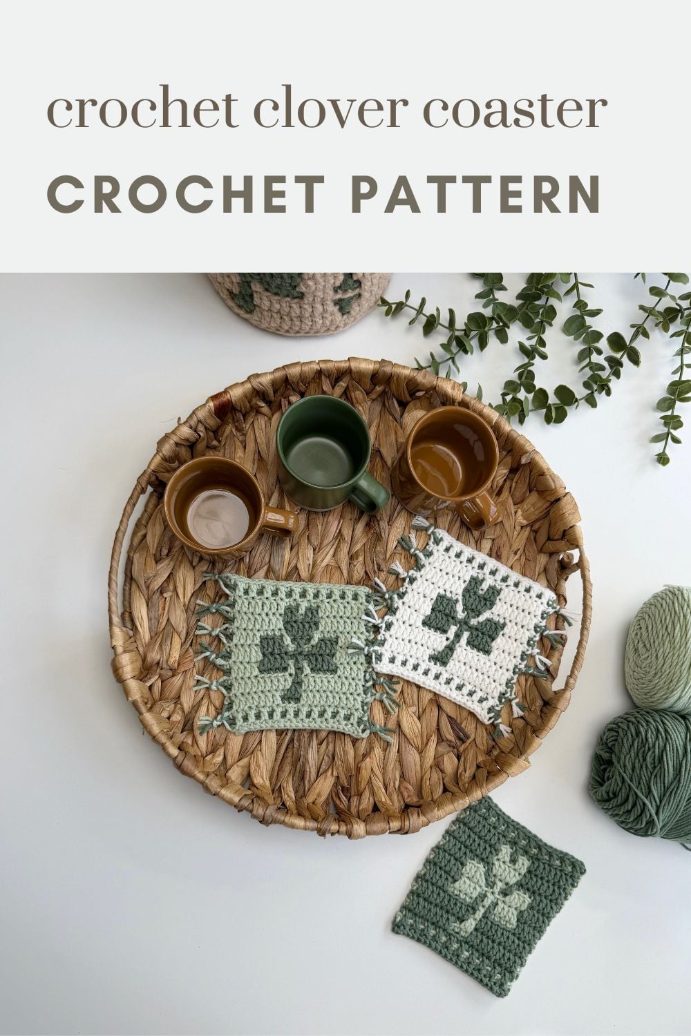 A woven tray holds three mugs and two crocheted clover coasters, with yarn and a finished crochet shamrock coaster nearby; text reads "crochet clover coaster CROCHET PATTERN.
