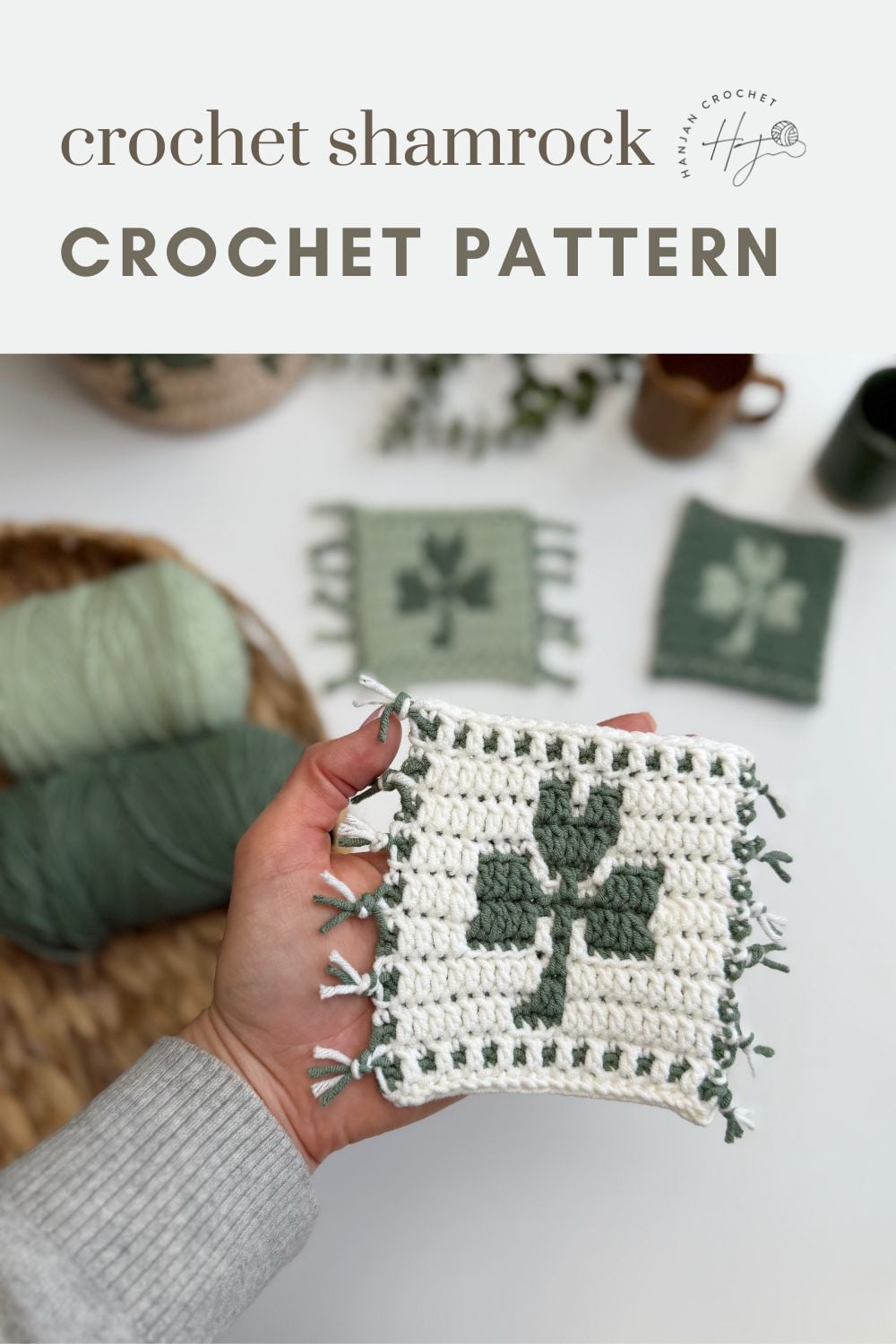 Person holding a crocheted square with a green shamrock design and fringe, plus yarn and finished squares in the background. Text reads "crochet shamrock coaster CROCHET PATTERN.