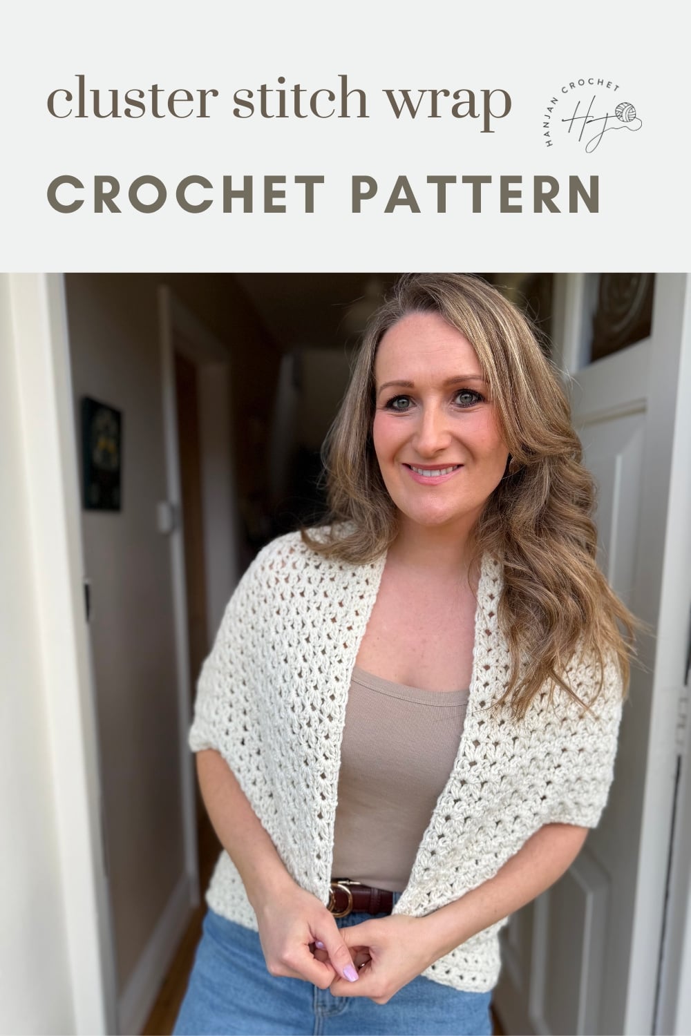 A woman stands indoors wearing a white crochet wrap over a beige top and jeans. Text above reads "cluster stitch wrap CROCHET PATTERN.