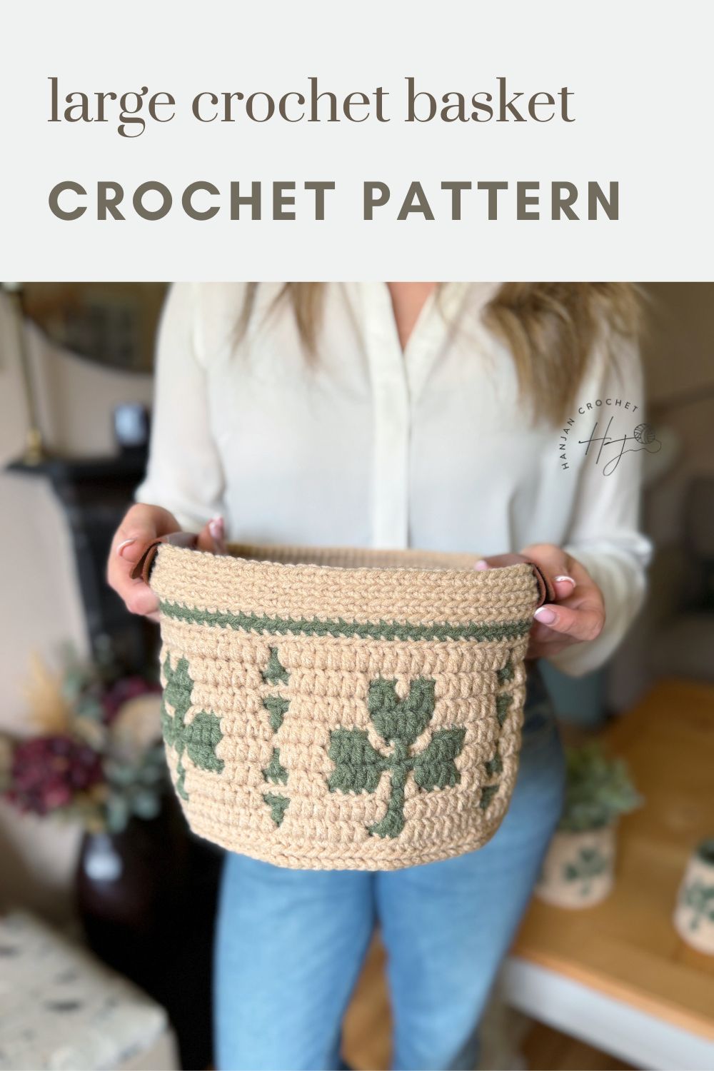 Person holding a large, beige crochet basket with green leaf patterns; text above reads "large crochet basket CROCHET PATTERN.
