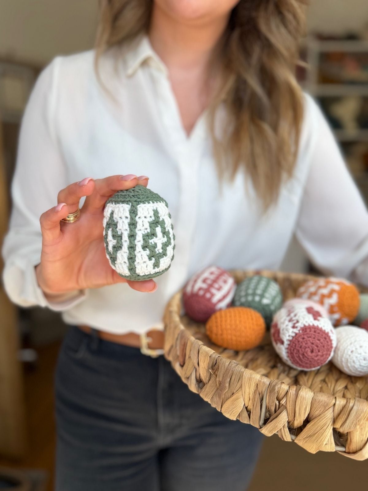 A person in a white shirt holds a crochet egg and a woven basket filled with various colored eggs, showcasing an adorable Easter Egg crochet pattern.