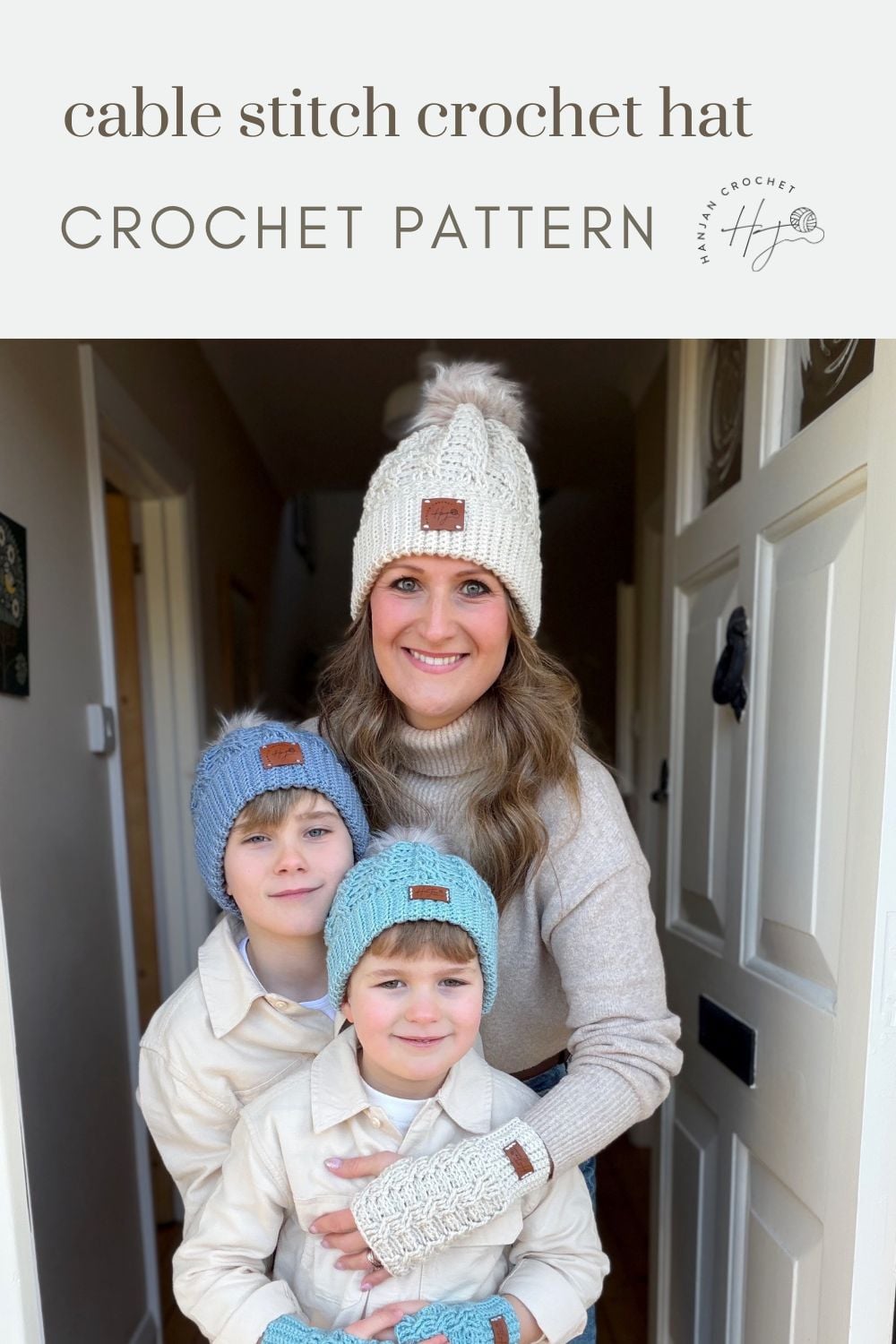 A woman and two children wearing matching cable stitch crochet hats and sweaters stand in a doorway, smiling at the camera, showing off their creations from a free crochet cable hat pattern.