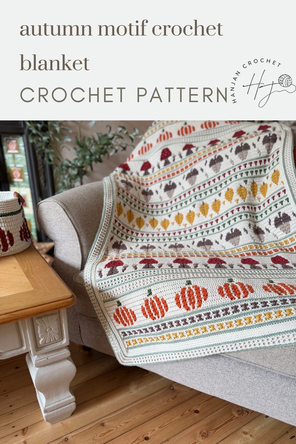 Crocheted blanket with autumn motifs draped over a gray sofa, featuring pumpkins, acorns, and leaves in orange, yellow, brown, and green.
