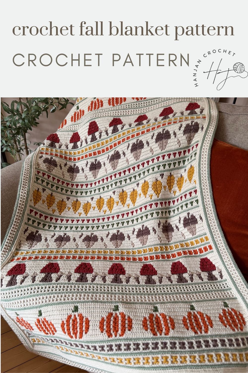 A crocheted blanket with rows of autumn-themed motifs, including pumpkins, leaves, and mushrooms in orange, yellow, brown, and green on a cream background.