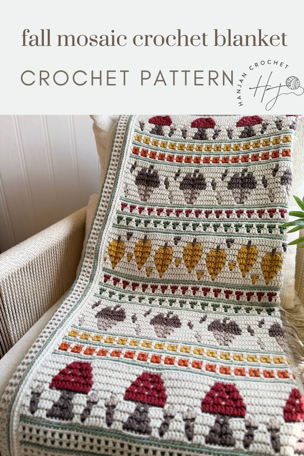 A crocheted blanket with rows of red mushrooms, yellow leaves, and geometric shapes in autumn colors draped over a chair.