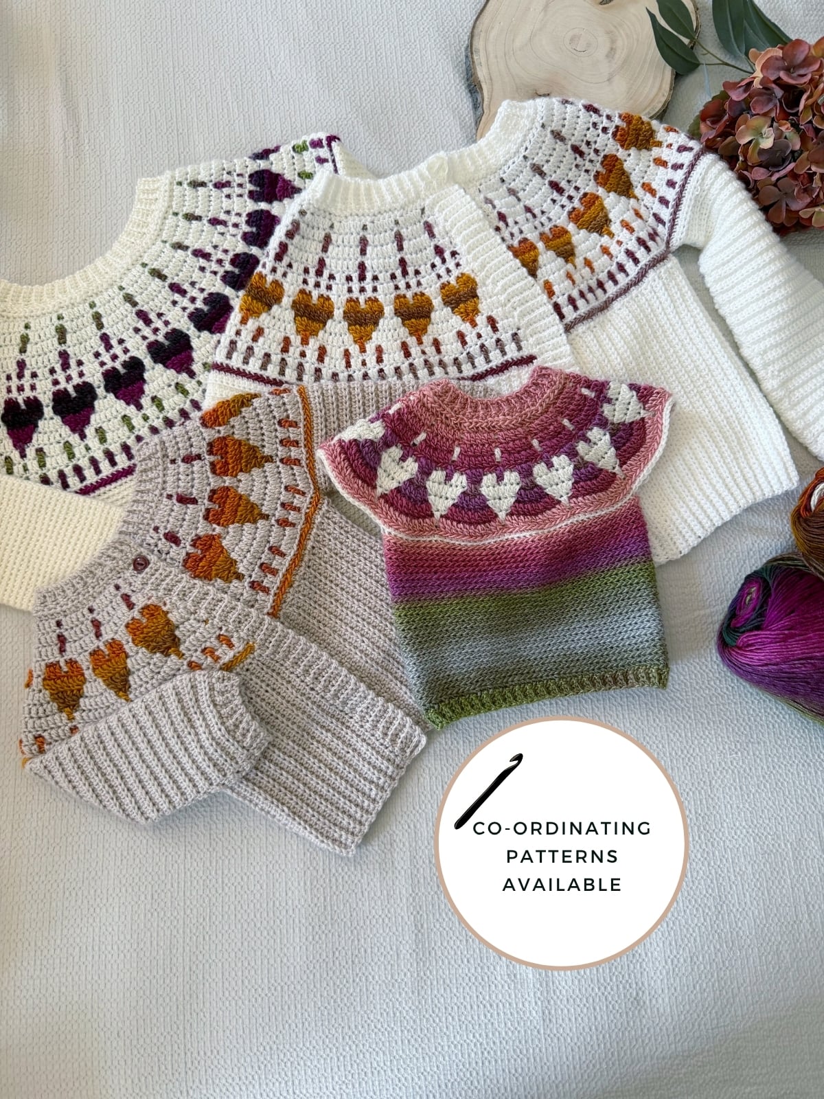 Four crochet sweaters with colorful yoke patterns and one small sleeveless top are arranged on a surface with yarn and flowers nearby. A circle reads “Co-ordinating patterns available.” Discover charming options, including a baby crochet sweater pattern, perfect for your next handmade project.