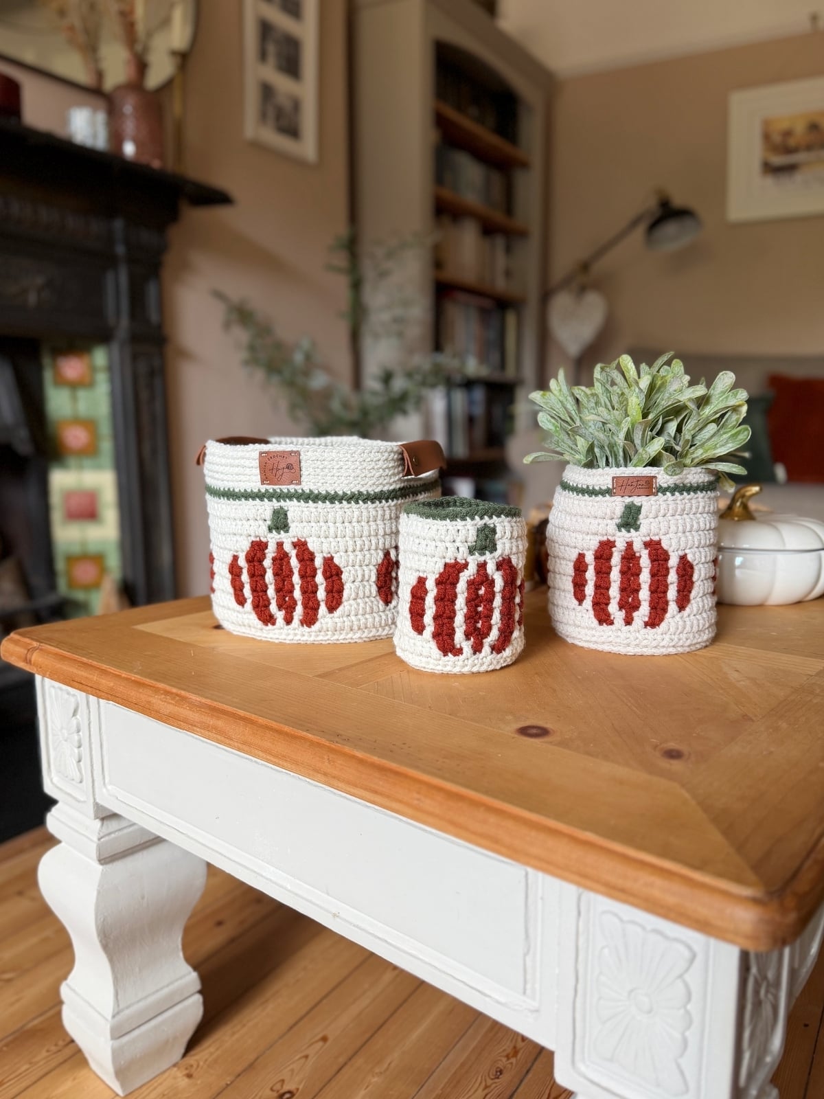 Three crocheted containers with pumpkin designs, including a charming crochet pumpkin basket, are displayed on a wooden coffee table in a cozy living room setting.