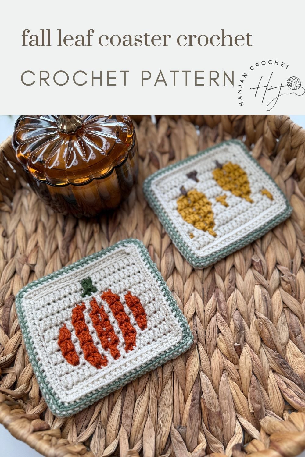 Two square crocheted coasters with fall motifs—a pumpkin and two leaves—on a woven tray, next to a glass pumpkin-shaped jar.